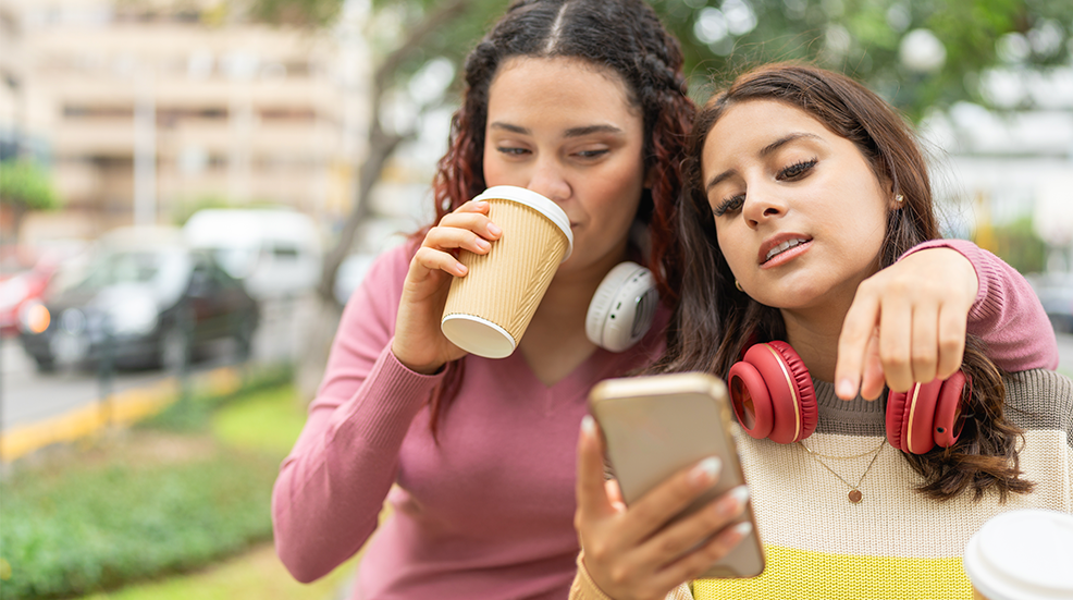 Women drinking coffee and using the mobile phone outdoors